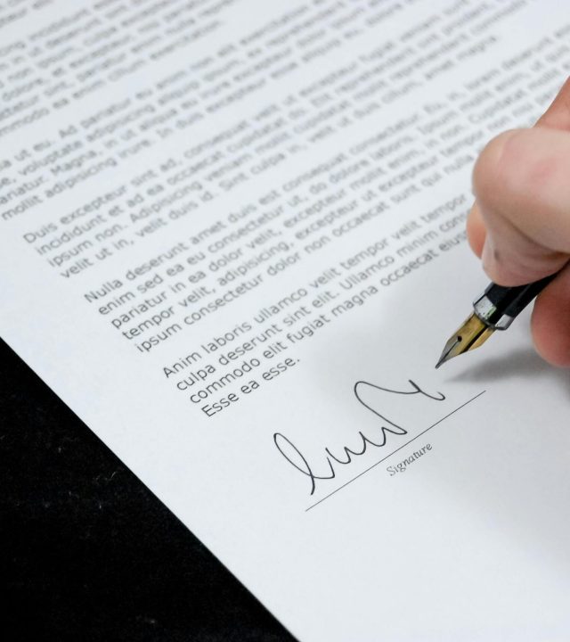 Close-up of a hand signing a formal document with a fountain pen, indicating agreement.